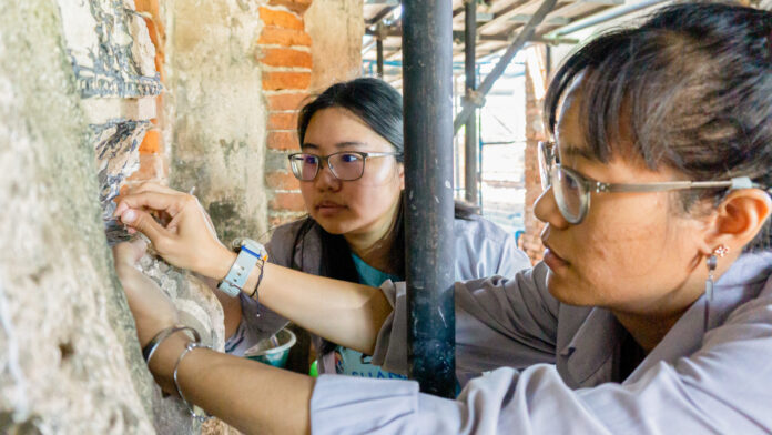 1022itn03 A local conservator teaches a Thai student intern techniques to preserve a 17th century Buddha statue in Wat Chai. Photo courtesy of the World Monuments Fund