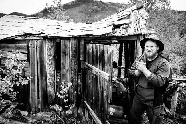 black and white photograph of park historian in front of a historic cabin black and white photograph of park historian in front of a historic cabin