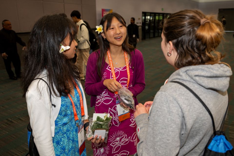 Finalists with flowers behind their ears smile while exchanging pins with another student.