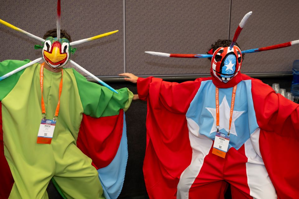 Two finalists in colorful outfits and masks pose at the pin exchange.