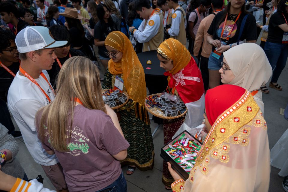 Finalists in colorful outfits exchange pins with one another.