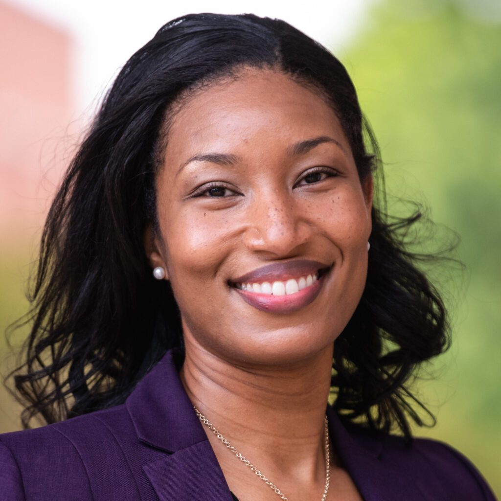 A smiling woman wearing a purple suit and silver necklace