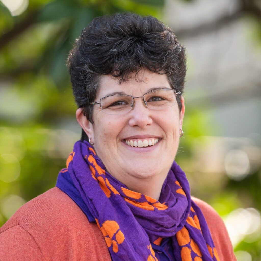 A smiling woman with glasses and a purple and orange Clemson scarf