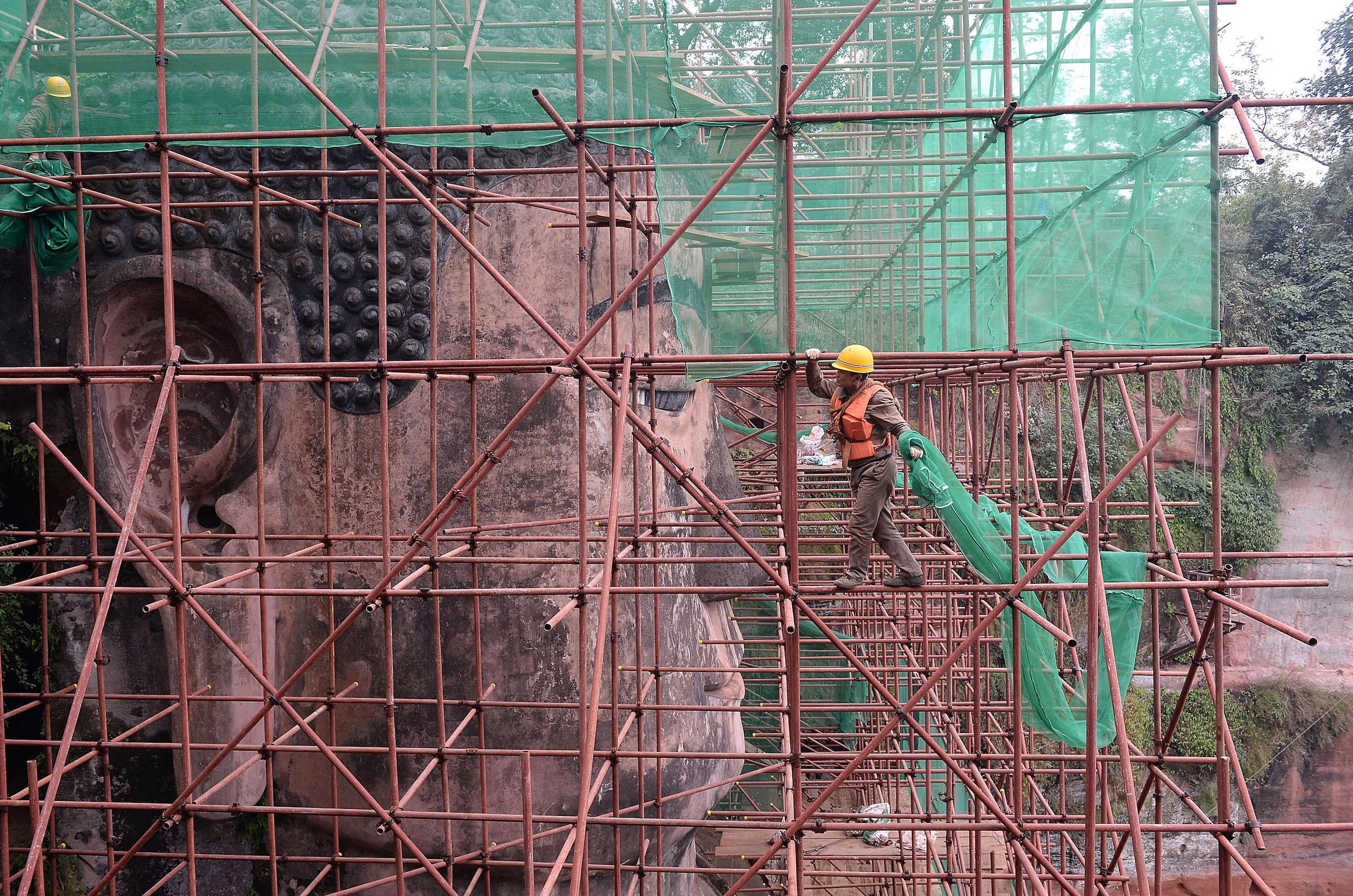 A man climbs across scaffolding around a giant statue of a buddha