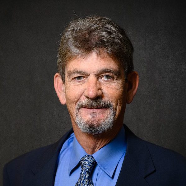 A man wearing a dark suit, blue shirt and blue tie