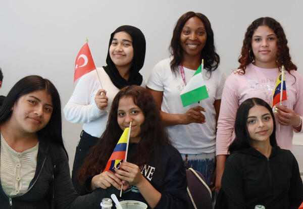 Five students and their teacher pose with small flags of their countries of origin