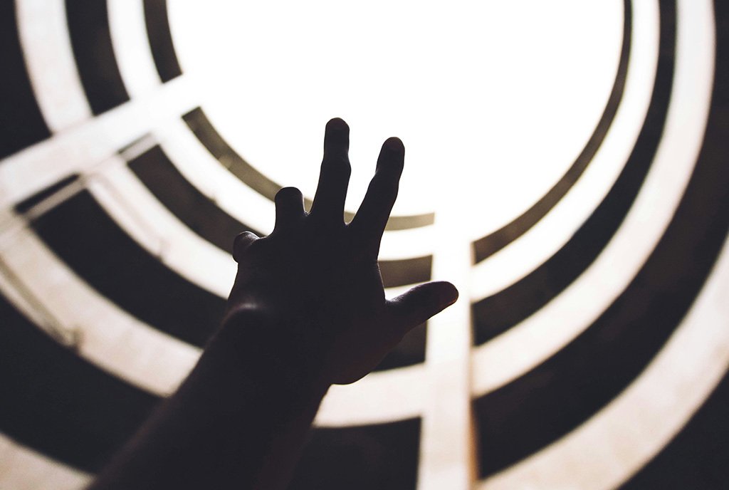 A hand reaches upwards, towards a lit opening from within a tunnel.