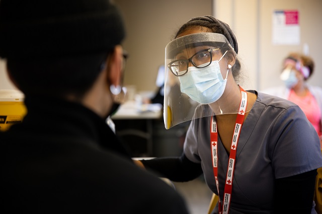 Woman in scrubs and PPE wearing a Red Cross lanyard