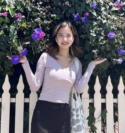 A woman smiling in front of a fence and flowers
