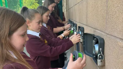 Roger Beech A group of children in red school jumpers locking their phones in boxes