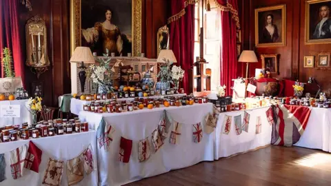 Hermoine McCosh  Tables with white clothes and old-fashioned Union Flag bunting with hundreds of jars of marmalade on them.