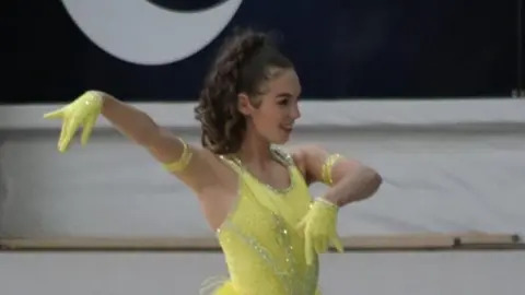 Moonrakers RSC A girl with brown hair in a yellow dress and yellow gloves dancing