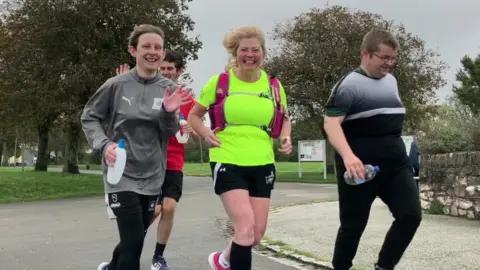 BBC A group of four runners wearing sports attire while out for a jog in a park in Plymouth.