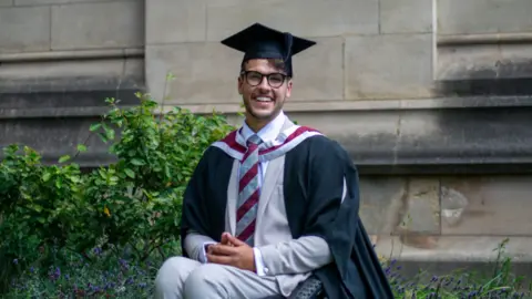 PA Media/University of Bristol Xander Van der Poll in his graduation robes and hat, sat in his wheelchair smiling outside a university building