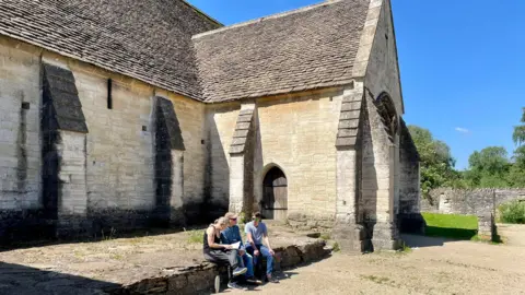 Andrew Morrison Three people sitting outside of the Tithe Barn during a sunny day