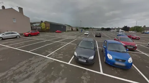 Google Central car park is a large, but sparse car park. There are houses and single-storey businesses surrounding the car park.