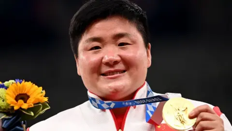 Getty Images China's Gong Lijiao celebrates on the podium with her gold medal after wining the women's shot put event during the Tokyo 2020 Olympic Games at the Olympic Stadium in Tokyo on 1 August 2021.