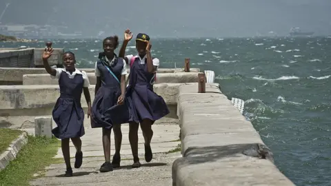 Getty Images Schoolgirls wave while walking at Kingston harbour (pictured August 2012)
