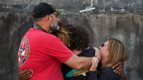 Reuters Three people hug each other at a vigil