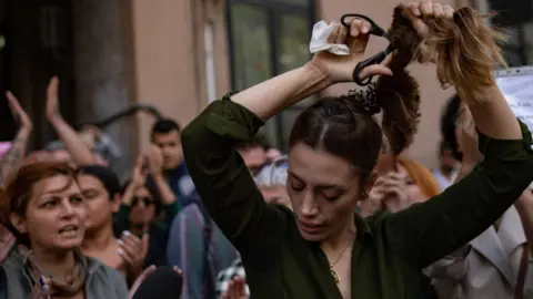 Getty Images Nasibe Samsaei, an Iranian woman living in Turkey, holds up her hair after cutting it off with a pair of scissors, during a protest on September 21, 2022