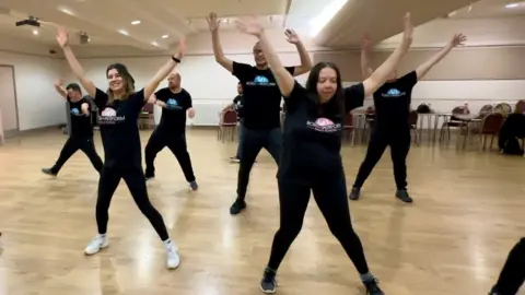 Carroll Weston/BBC Women in black outfits dancing with arms upwards
