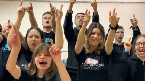 Carroll Weston/BBC Young men and women with black t-shirts holding their arms up