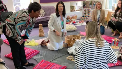 Martin Heath/BBC Fatima Whitbread bends down to talk to mothers kneeling on a play mat