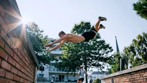 Wizzy Gang Man jumping between buildings with his arms outstretched