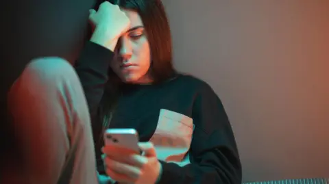 Getty Images A morose looking teenager stares at a smartphone