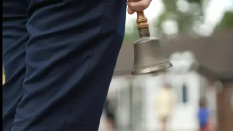 BBC A teacher carrying a school bell