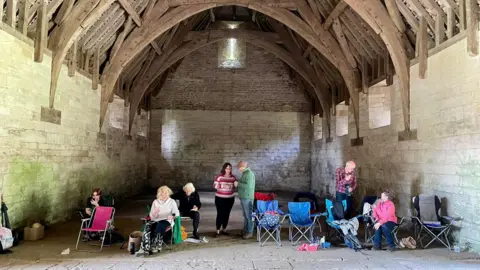 Andrew Morrison The Bradfordians Dramatic Society standing in the Tithe Barn. There are high arched wooden beam ceilings and stone slabs on the floor.