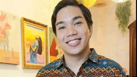 Facebook/OfficialBenPablo Ben Pablo, wearing a colourful shirt, smiles for a photo posted on his Facebook page. In the backdrop, paintings and a plant can be seen.