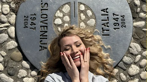 Luca Fornasier Singer Tish lying down on rocky pavement with a metal marker on the ground (Credit: Luca Fornasier)