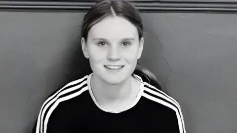 Family handout Black and white picture of Holly. She is sitting with her back against a wall and is smiling at the camera