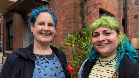 Tara Dolby/BBC Two women looking at the camera - one on the left wears a navy jacket and has blue colour in her hair - the one on the right wears a stripey top and has vivid blue and green colour in her hair