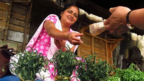 Getty Images Darjeeling, india. Saleswoman accepting money for the sale of fresh herbs in her market stall. April 2012