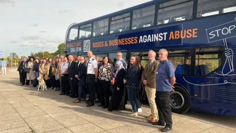 Emma Baugh/BBC A group of people standing in front a bus sign-written with a "buses against abuse" sign.