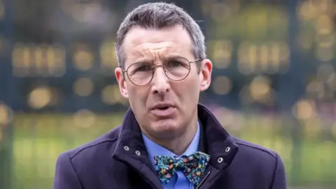 PA Media The environment minister Andrew Muir, wearing glasses, a navy jacket with a bow tie and collar up.