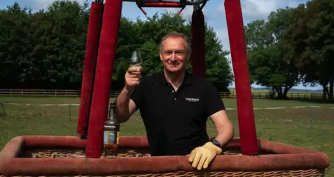 PA Media Sir David holding a glass of whisky in a hot air balloon