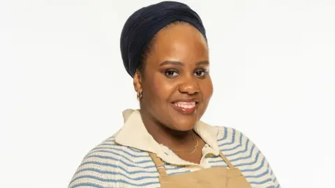 Channel 4/Love Productions/Mark Bourdillon Illyin Morrison wearing a blue and cream striped jumper and a brown baking apron. She is smiling towards the camera.