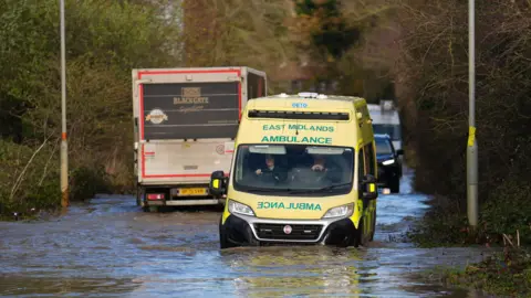 PA Media An ambulance drives through floodwater near the Billing Aquadrome in Northamptonshire.