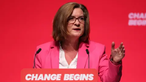 EPA Eluned Morgan speaking at Labour conference in front of a banner that says "Change Begins". She is wearing a pink suit with a white shirt.