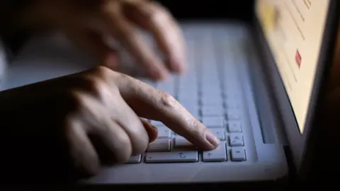 PA Media A person's hands type on a white laptop keyboard while looking at a website.