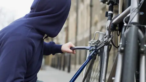 Getty Images A person in a blue hoodie attempts to chop off a bicycle lock with bolt croppers.
