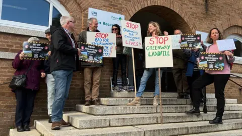 BBC People standing on the steps of County Hall in Exeter with signs protesting against the proposed landfill site