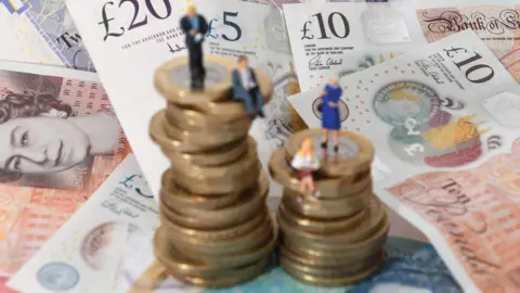 PA Media Models of men and women on a pile of coins and bank notes.