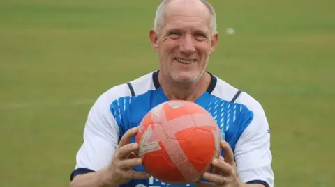 Paddy Berryman Roy wearing a blue and white jersey holding an orange football smiling for the camera 