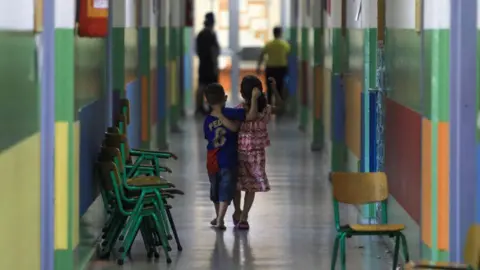 Getty Images Two children walk arm in arm down a long, colourful corridor