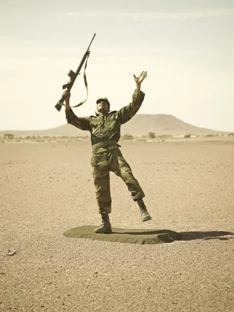 Simon Thorpe A soldier outdoors posing with his hand and gun towards the sky
