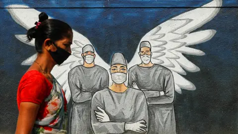 Reuters Mask-wearing individual passes a mural